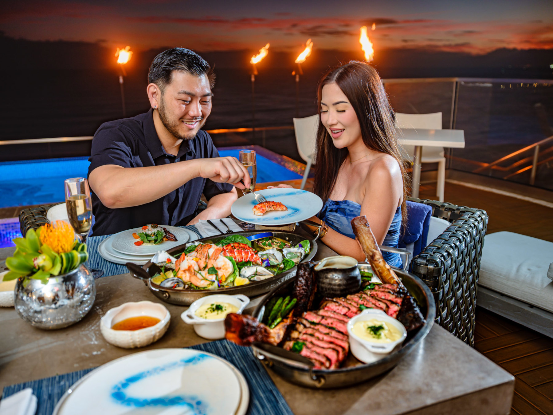 Couple enjoying dinner together with shrimp, lobster tails, oysters and steak